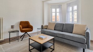 Ein modernes Wohnzimmer mit einem grauen Sofa, einem Holztisch und einem orangefarbenen Sessel.