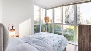 A bedroom with a large window, a bed with a floral bedspread, a floor lamp, and a wooden headboard. - Luxury 2-bedroom condo beach side Yaletown (Vancouver)