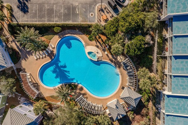 An aerial view of a swimming pool surrounded by palm trees and lounge chairs, with a parking lot and buildings in the background. - Walk To The Beach! Gated Community, Pool, Sea-La-Vie (Miramar Beach)