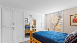 Une chambre à coucher avec un lit en bois, une grande armoire et une fenêtre donnant sur des arbres.