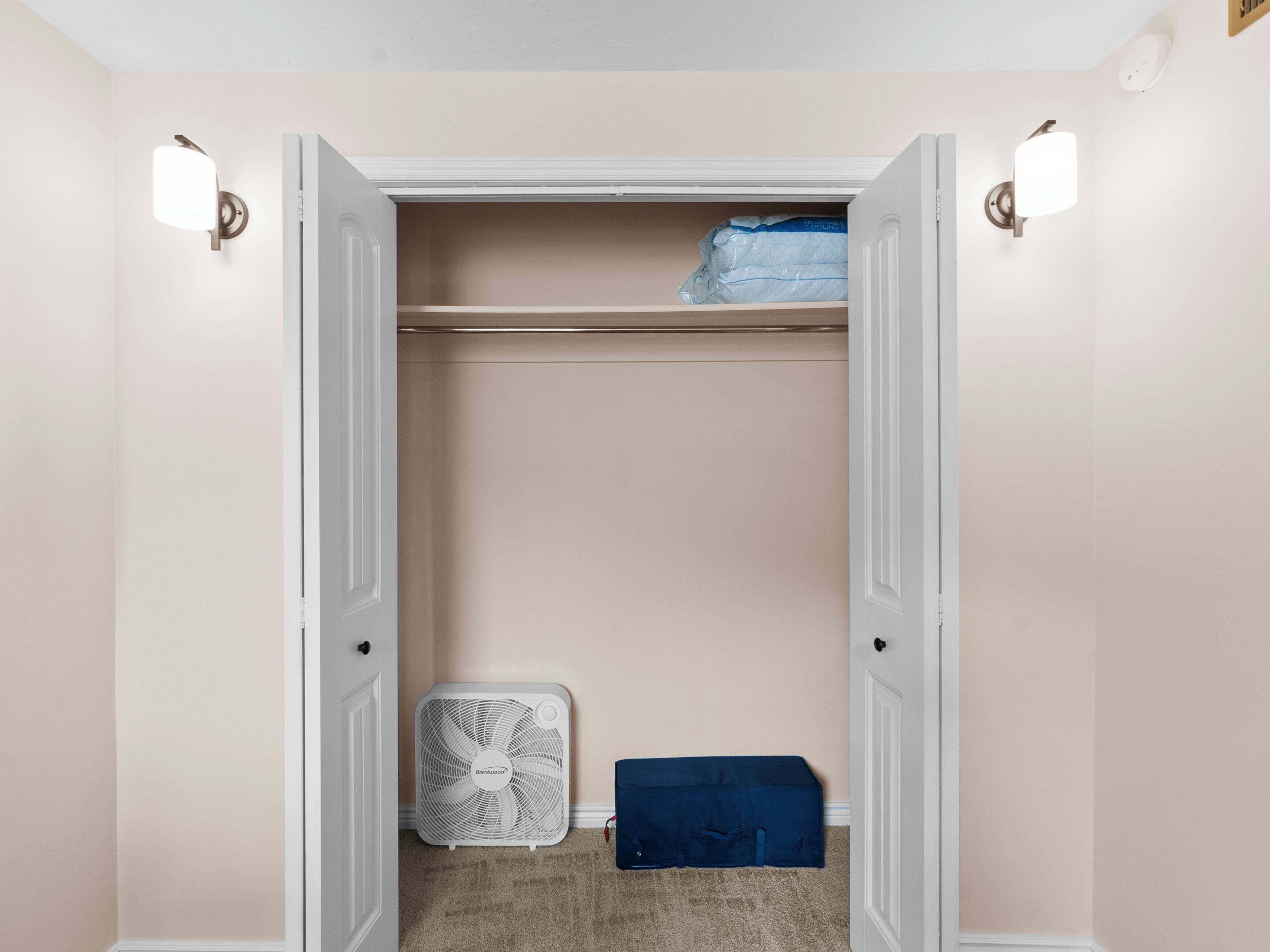 A walk-in closet with a white door, a white fan, and a blue storage box.
