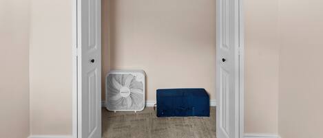A walk-in closet with a white door, a white fan, and a blue storage box.
