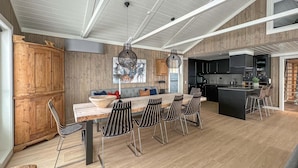 A modern kitchen with a central island, wooden cabinetry, and a dining area with a long table and chairs. - Nice home in Gålå with sauna (Gålå)
