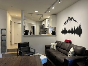 Ein modernes Wohnzimmer mit Ledersofa, Esstisch und einer Küche im Hintergrund.