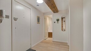 A hallway with white walls, a wooden ceiling beam, a white door, a framed picture, and a mirror with a hanging plant. - GuestReady - Historic Cavern Quarter gem (Liverpool)
