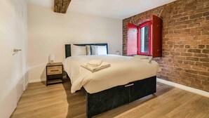 A bedroom with a bed, bedside table, lamp, and a brick wall. - GuestReady - Historic Cavern Quarter gem (Liverpool)