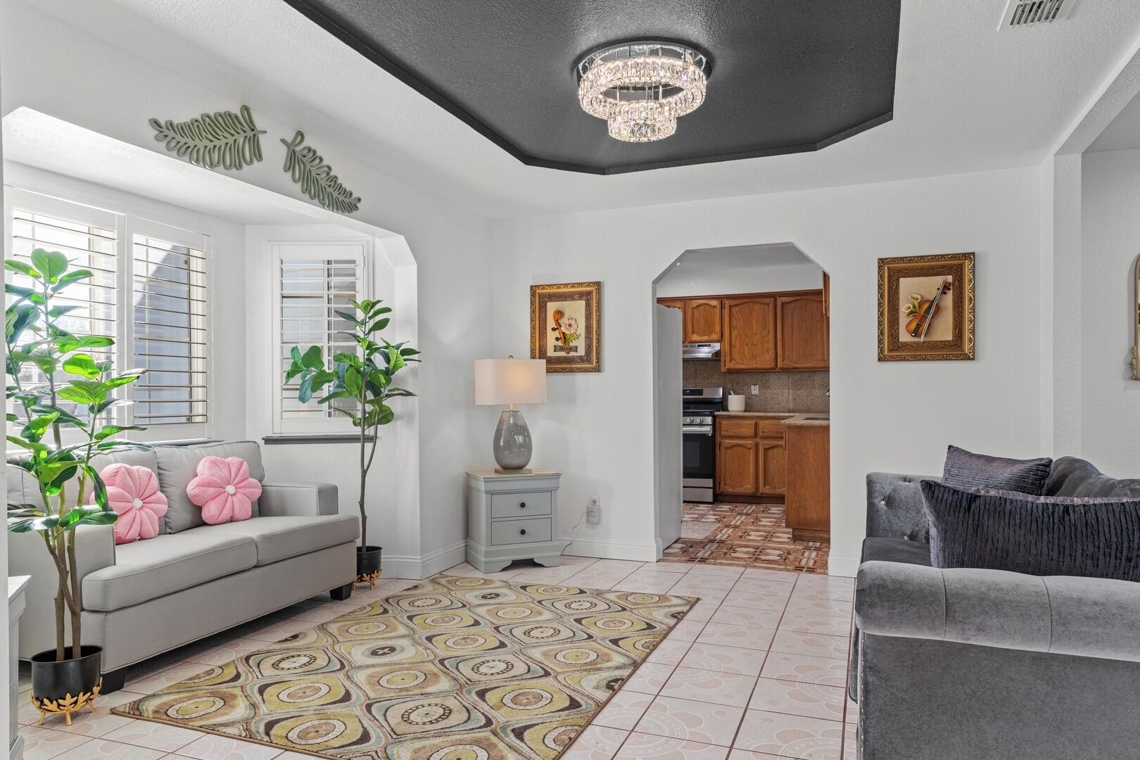 A living room with a grey sofa, a patterned rug, a small table with a lamp, and a chandelier.