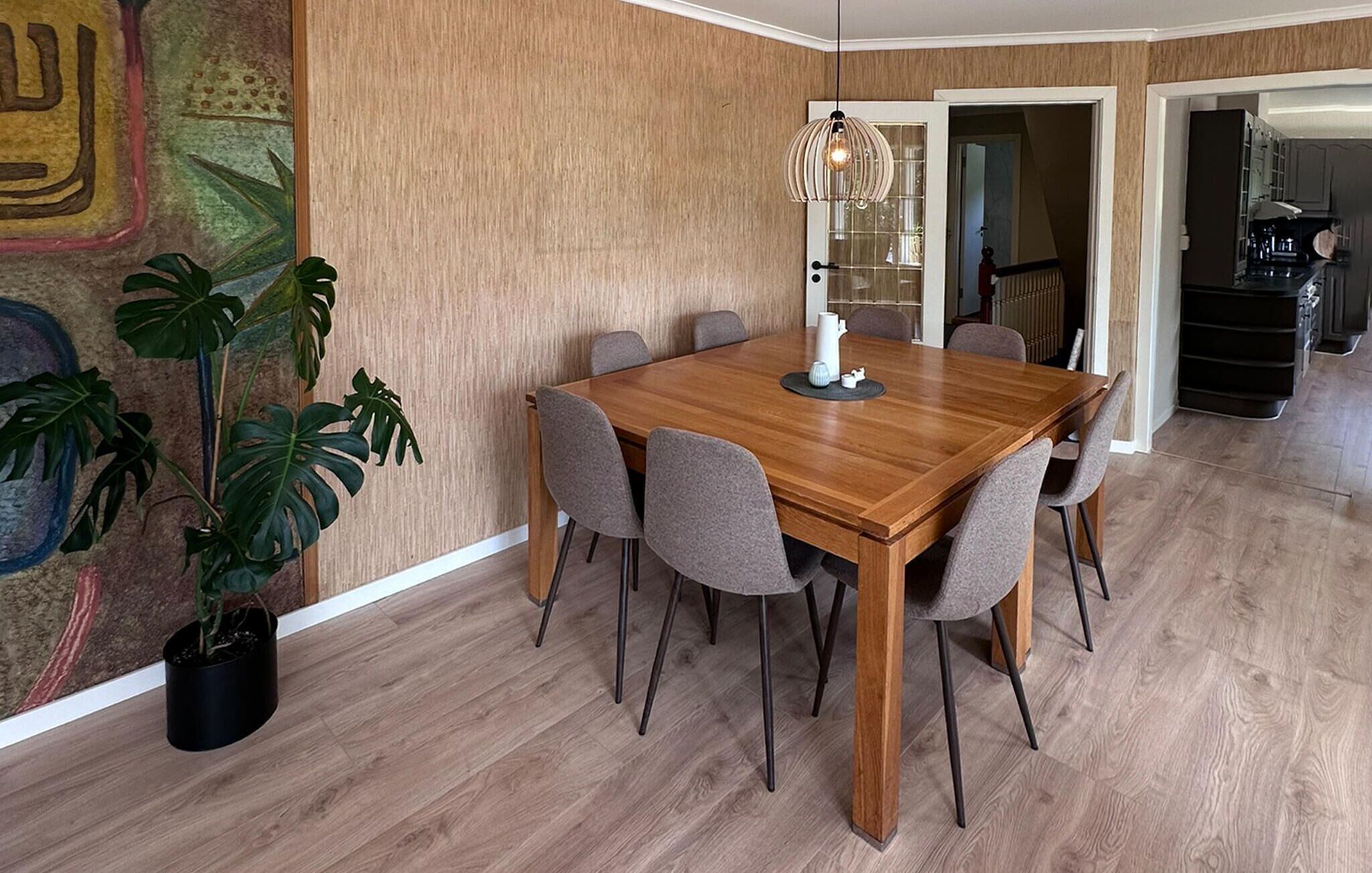 A dining area with a wooden table and six chairs, a potted plant, and a decorative light fixture.