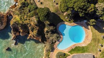Vue aérienne d’une propriété située sur la côte, avec une piscine, des falaises rocheuses et une végétation luxuriante.