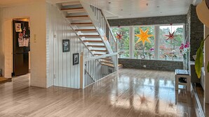 A spacious living area with a wooden staircase, a stone accent wall, and large windows with star decorations.