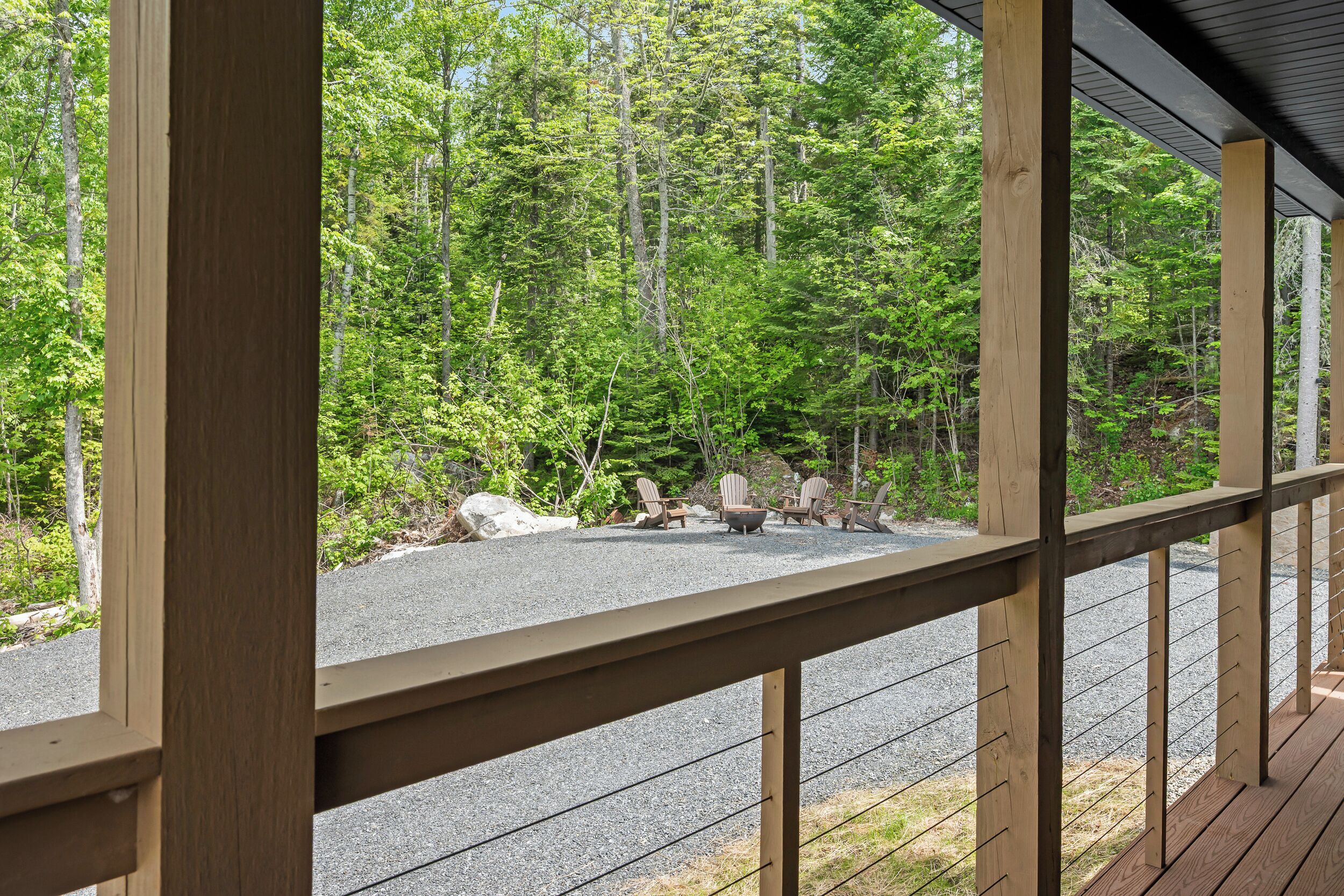 Une terrasse en bois avec un chemin de gravier, entourée d’une forêt dense.