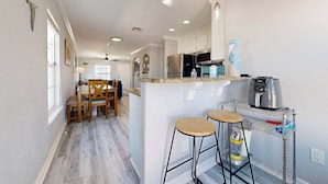 A modern kitchen with a central island, bar stools, and a stainless steel refrigerator. - Feelin Beachy, Shared Pool, Walk to the Beach (Port Aransas)