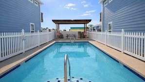 A rectangular swimming pool with a wooden deck and a covered seating area in the center. - Feelin Beachy, Shared Pool, Walk to the Beach (Port Aransas)