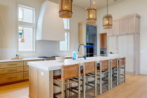A modern kitchen with a central island, wooden chairs, pendant lighting, and built-in cabinetry. - SBSL724 Ocean View, Private Heated Pool, Golf Cart Included, Boardwalk to the Beach (Port Aransas)