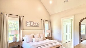 A bedroom with a large bed, bedside tables, a bench, a mirror, and a sign on the wall. - 5BR Lakefront Retreat — Quiet Cove, Large Private Dock & Easy Boat Access (Bremen)