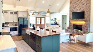 A spacious kitchen with a large island, a brick fireplace, and a flat-screen TV mounted above it. - 5BR Lakefront Retreat — Quiet Cove, Large Private Dock & Easy Boat Access (Bremen)