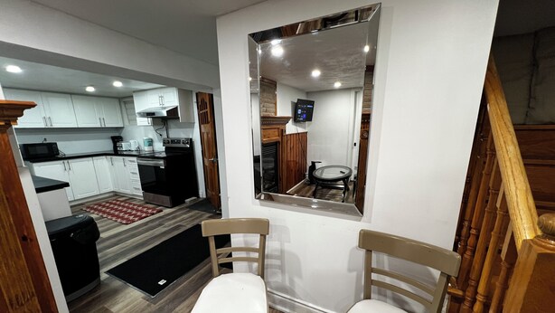 A compact kitchen with white cabinets, a microwave, and a stove. There are two wooden chairs with white cushions in a small seating area. - Prime Location 3Bedrooms, 2 Bath,Basement Apt with free parking-Close to Transit (Mississauga)