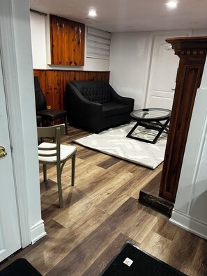 Una habitación con un sofá negro, un armario de madera, una mesa de vidrio y una alfombra estampada.