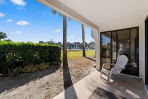 A covered outdoor area with a white chair, a glass door, and a view of a building complex in the background. - Spacious 3BD/3BA Edgewater Beach Villa (Panama City Beach)