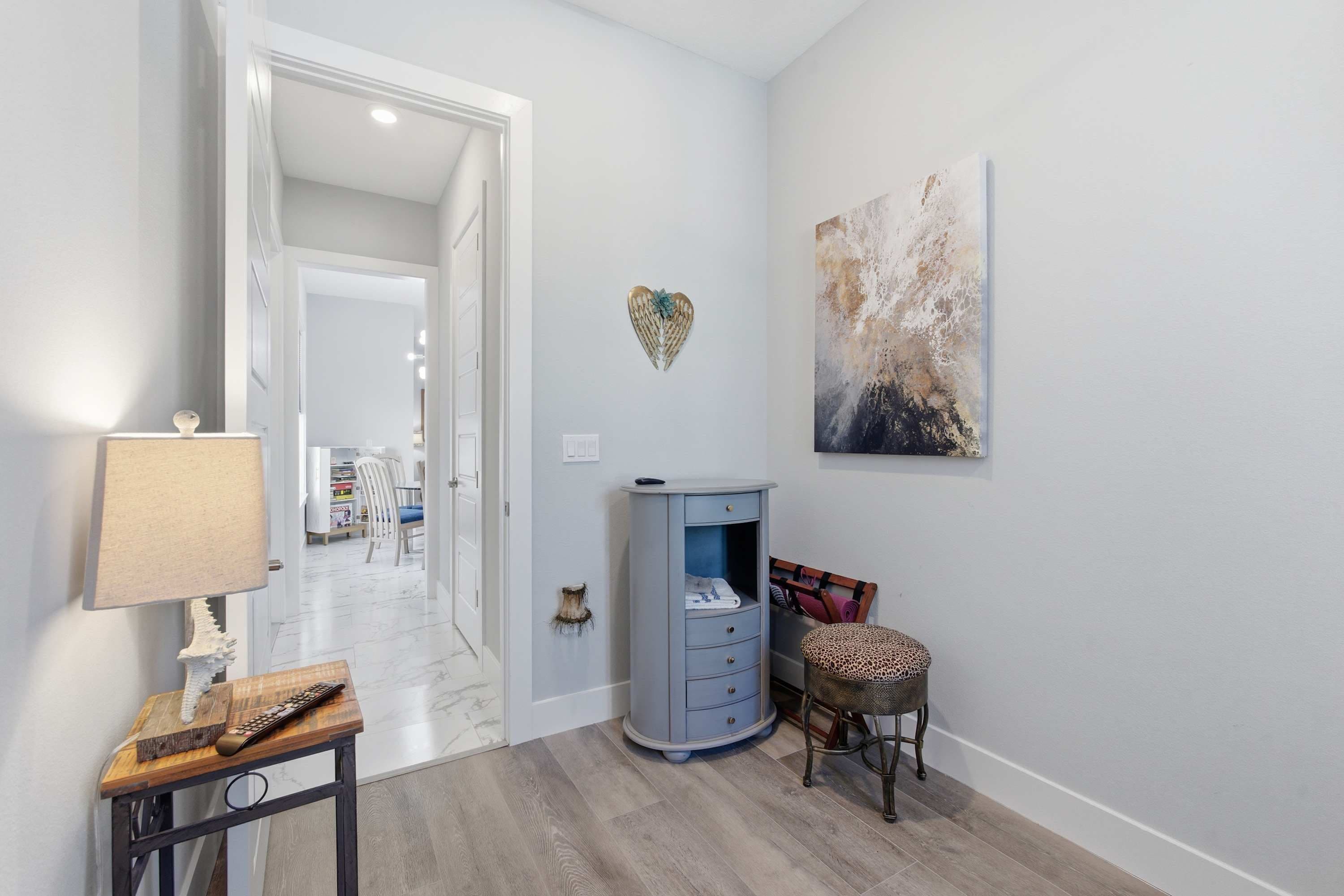 Un pasillo con una consola de madera, una lámpara, un armario azul, una silla y una decoración con forma de corazón en la pared.