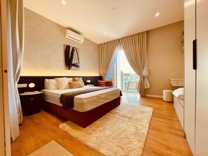 A modern bedroom with a large bed, a bedside table, a nightstand, a wall-mounted air conditioner, and a view of the outside through a large window. - Quill Residence 1 Bedroom Apartment (Kuala Lumpur)
