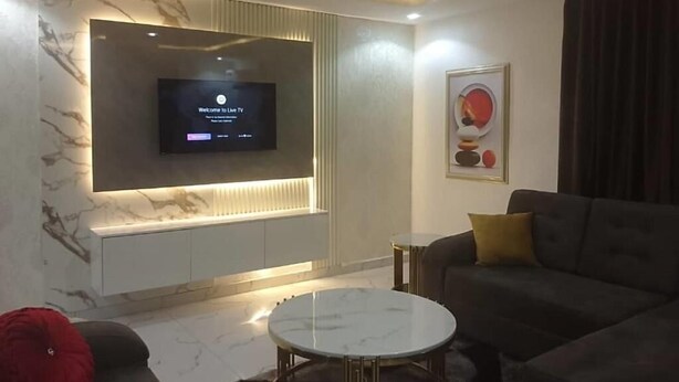 Un salon moderne avec un téléviseur à écran plat fixé sur un mur en marbre, un canapé, une table basse et une petite table d’appoint.