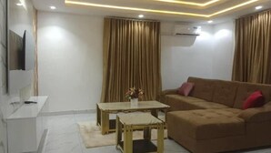 Un salon moderne comprenant un canapé, deux tables d’appoint, un téléviseur à écran plat et un plafond doté d’un éclairage encastré.