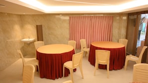 Una sala de conferencias con dos mesas redondas, sillas color beige, un lavamanos y una cortina.