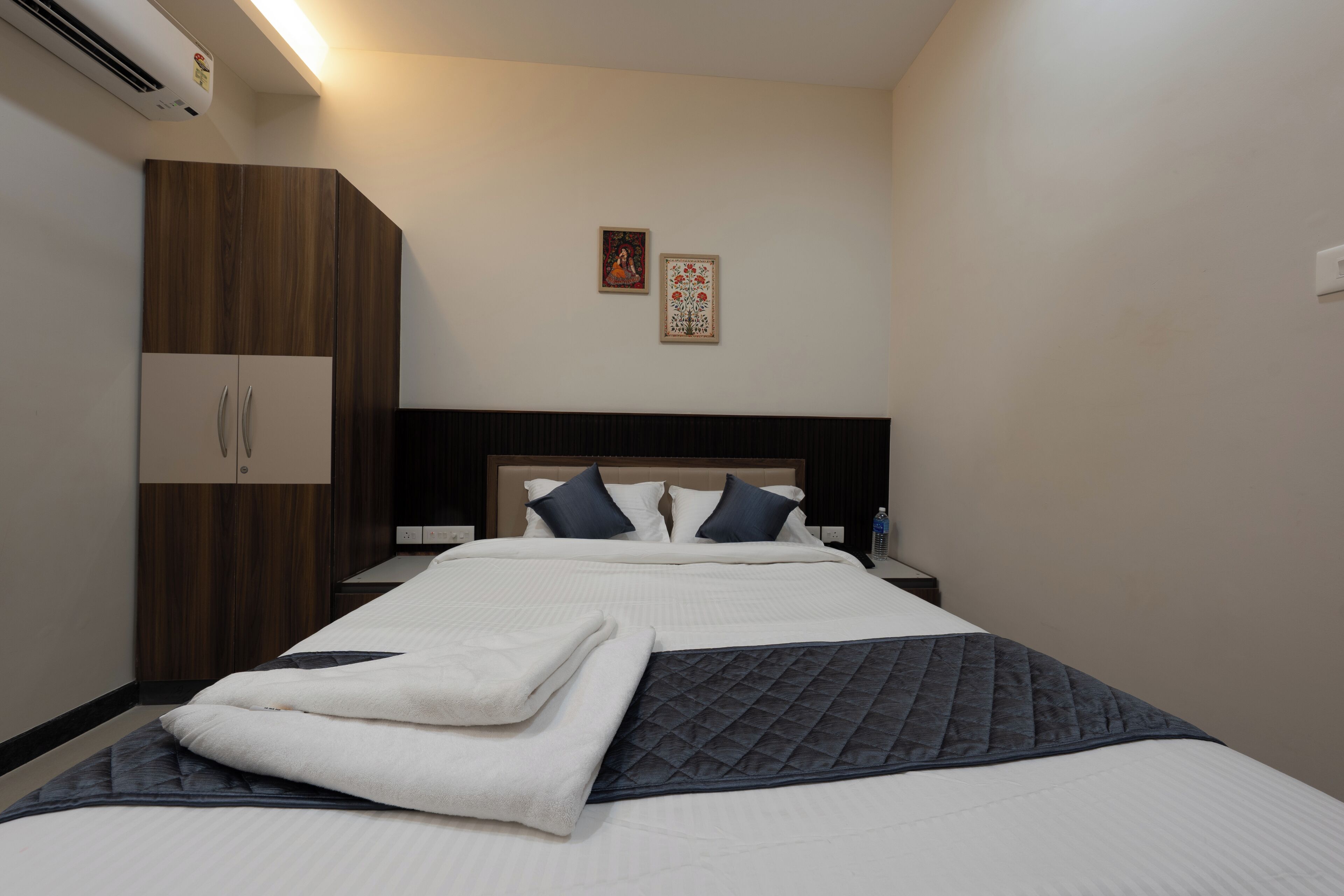 Una cama bien hecha con un edredón acolchado, un armario de madera y dos cuadros colgados en la pared.