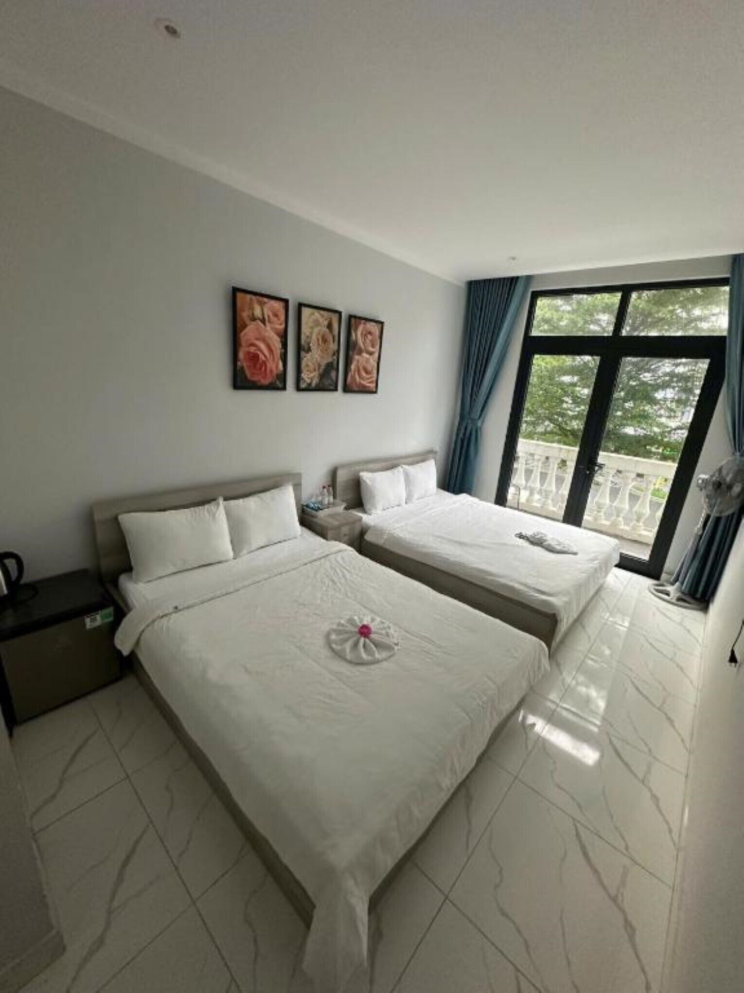 Une chambre d’hôtel avec deux lits, une table de chevet, une fenêtre avec des rideaux et un balcon donnant sur une vue agréable.