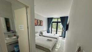 Une chambre d’hôtel avec deux lits, une salle de bain avec un lavabo et un balcon avec des rideaux.