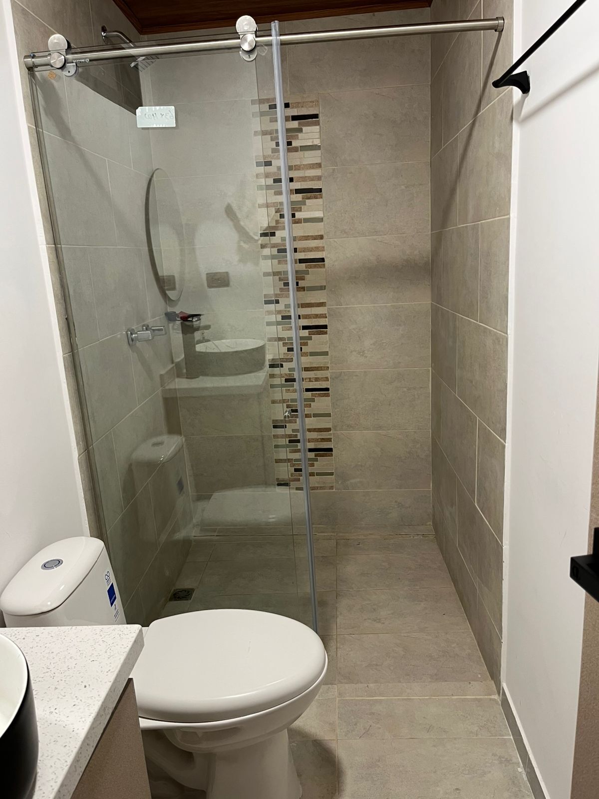A compact bathroom with a glass-enclosed shower, a toilet, and a sink.