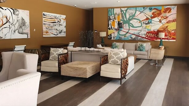 A spacious living room with a large sofa set, a coffee table, and a fireplace. There are abstract paintings on the walls and a large window providing natural light.