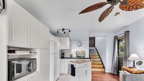 A modern kitchen with white cabinetry, a microwave, and a wooden island. There is a staircase leading to a loft area. - #57 Beautifully Remodeled Studio (Pahala)