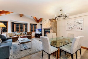 A living room with a fireplace, a glass-top dining table, and a television. - Ski In/Out at Gondola One Vail Slopeside Lodge 401 (Vail)