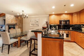 A modern kitchen with wooden cabinets, a granite countertop, and a built-in island with seating. - Ski In/Out at Gondola One Vail Slopeside Lodge 401 (Vail)