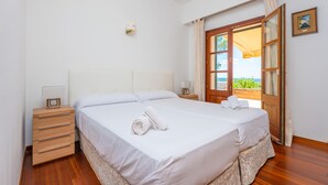Un dormitori amb un llit, taules de nit, cortines a la finestra i vistes a vegetació a l'exterior.