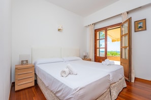 Ein Schlafzimmer mit einem Bett, Nachttischen, Vorhängen an einem Fenster und Blick auf Grün.