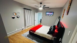 A bedroom with a bed, a ceiling fan, a TV, and a door leading to another room.