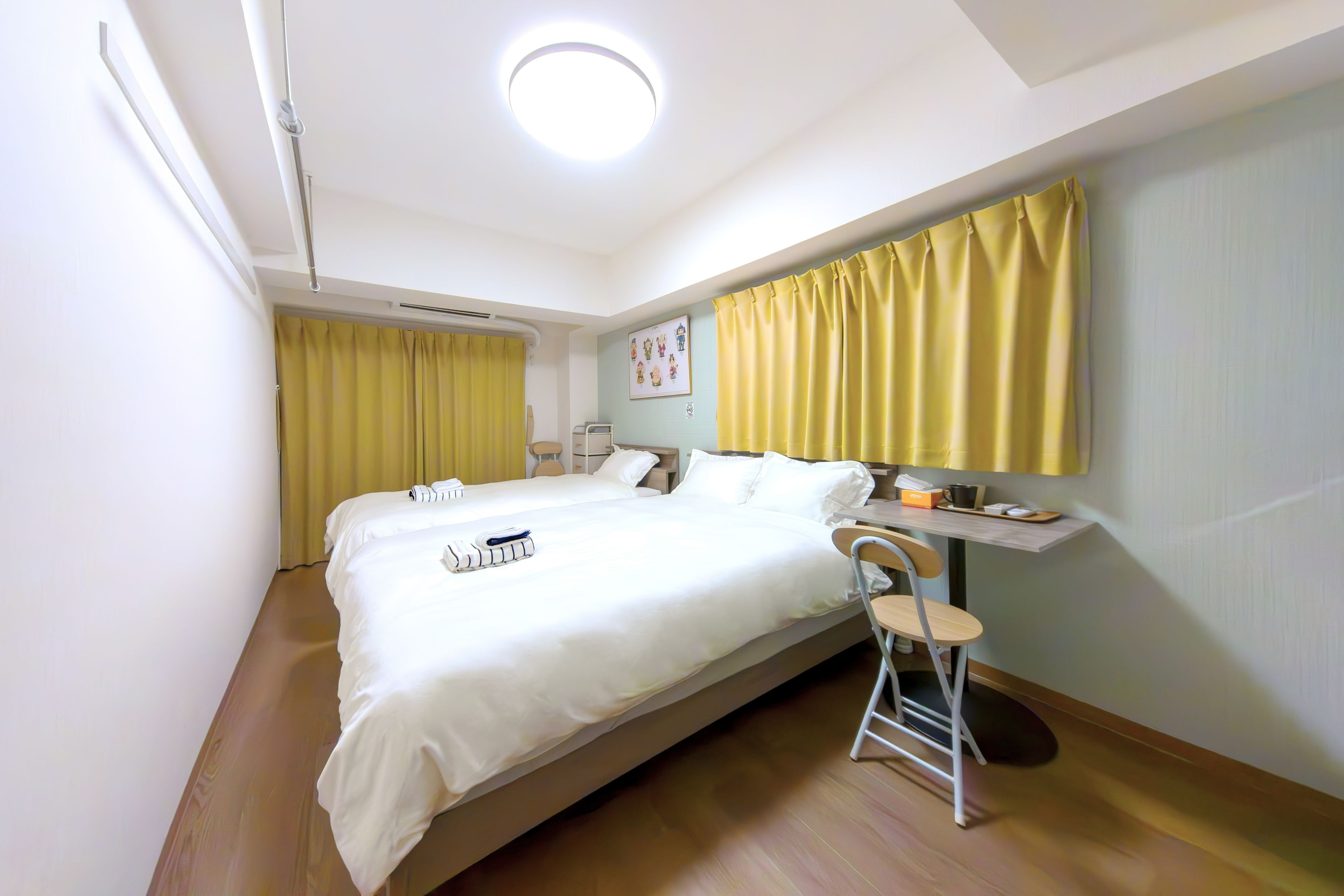 A hotel room with a large bed, a small table, a chair, and a wall-mounted shelf.