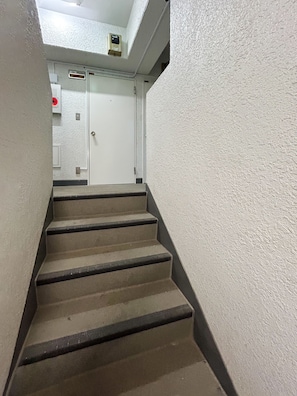 A staircase with a handrail leading to a door at the top. - Ikebukuro 5 Min by Train | 21㎡ for 3 | Double + Single Bed, Kitchen | Wi-Fi (板橋区)