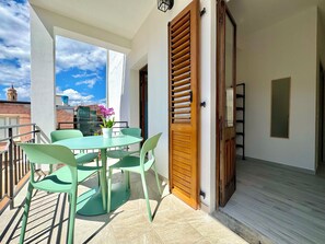A balcony with a table and chairs, a wooden door, and a view of buildings in the background. - "Le Corti Sarde Village" (Bari Sardo)