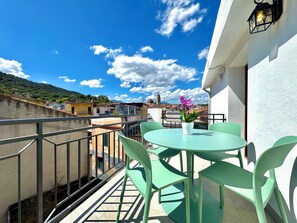 Un balcon avec une table et des chaises, un pot de fleurs et une vue sur des immeubles et une tour au loin.