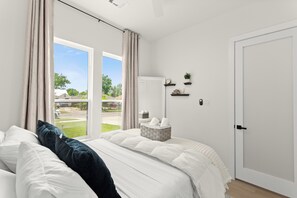 A bedroom with a bed, a window with curtains, a door, and a small shelf with items. - Spacious 5-bedroom house in lovely Dallas near airport and downtown. (Dallas)