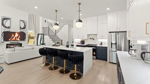 A modern kitchen with white cabinets, a central island, bar stools, a built-in oven, and a stainless steel refrigerator.