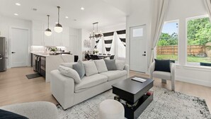 A modern living room with a sofa, coffee table, and a view of a garden through large windows.