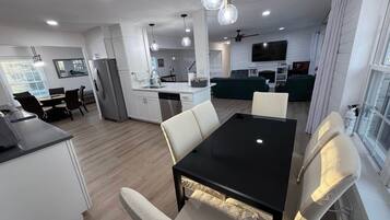 Una cocina moderna con armarios blancos, un comedor con una mesa negra y sillas blancas, y una sala de estar con un sofá verde.