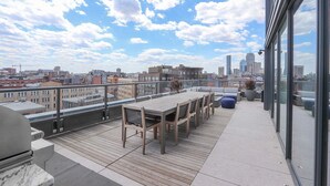 A rooftop terrace with a wooden table and chairs, a blue ottoman, and a city view. - Blueground | South End, pool, nr Boston Common (Boston)