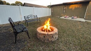A backyard with a fire pit, two metal chairs, and a white fence. - Relaxing 1-bedroom Apartment in beautiful Ormond Beach (Ormond Beach)