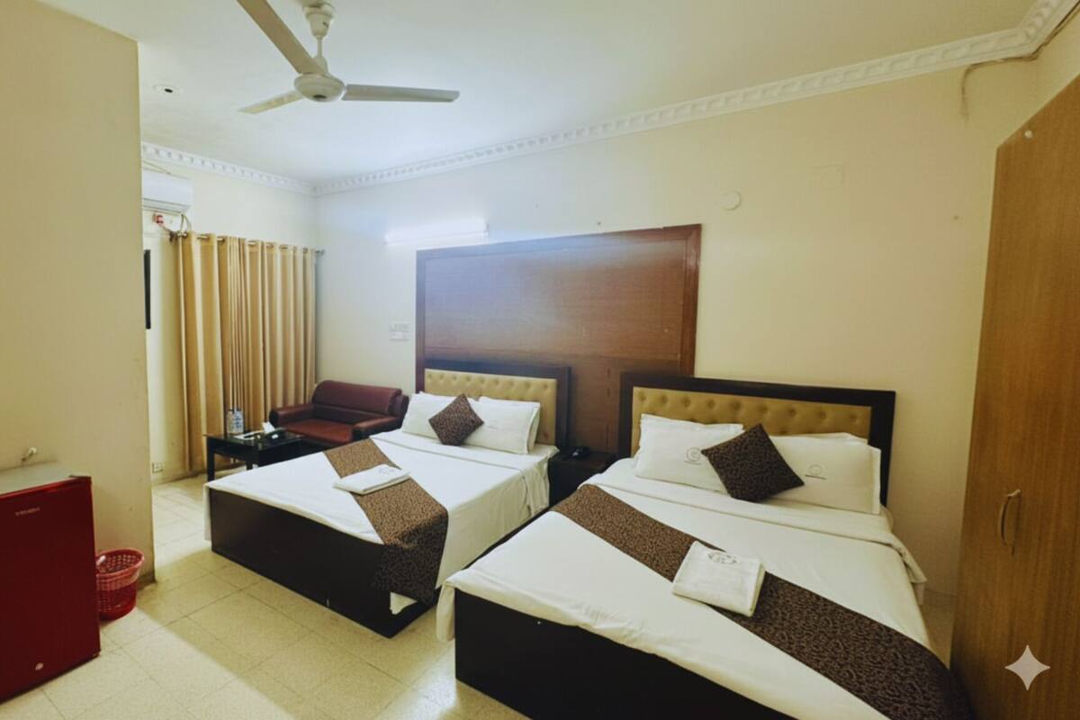A hotel room with two beds, a red cabinet, a ceiling fan, and a view of the outside through curtains.